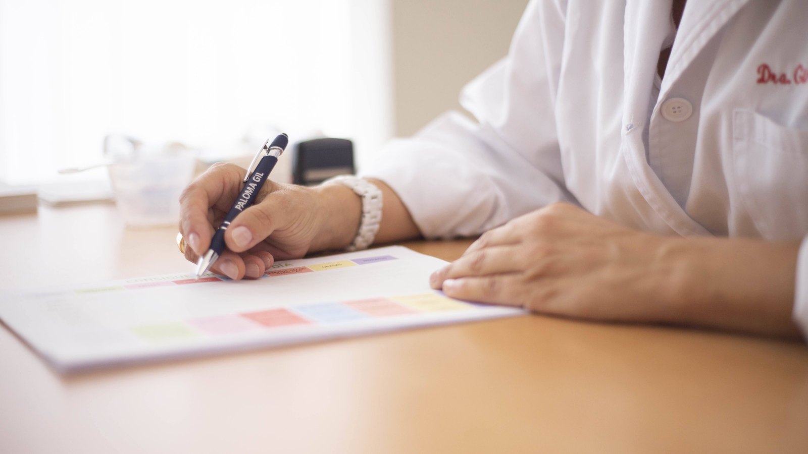 Médica escrevendo uma prescrição em uma mesa de atendimento